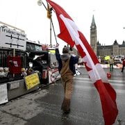 Un manifestant, devant le parlement, avec un drapeau du Canada.