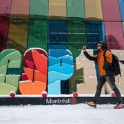 Un homme marche devant le logo de la COP sous la neige.