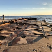 Une structure de métal est échouée sur le sable devant la mer.