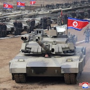Kim Jong-un, dont on ne voit que la tête, conduit un char d'assaut arborant un drapeau nord-coréen.
