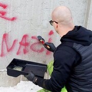 Un homme applique un produit liquide sur un graffiti antisémite afin de l'effacer.