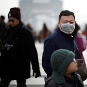 Parmi des touristes, un homme asiatique porte un masque.