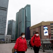 Deux femmes portant chacune un masque de protection marchent à l'extérieur, entourées de gratte-ciel.
