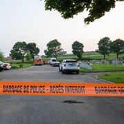 Des voitures du SPVQ ainsi qu'un camion de pompier dans une allée menant à un cimetière. Une banderole « accès interdit » flotte à l'avant de l'image.