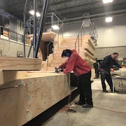 Des gens travaillent sur des morceaux de bois dans un hangar. 