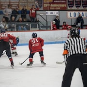 Des jeunes joueurs de hockey en action sur la glace sous l'oeil d'un arbitre.