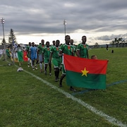 Des joueurs de l'équipe du Burkina Faso défilant avec en avant-plan le drapeau de leur pays.