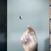 Une main pointe la trace laissée par un coup de feu dans une fenêtre.