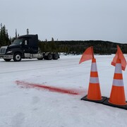 Deux cônes orange sont posés sur la neige. Au loin, un camion est stationné.