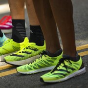 Gros plan sur les pieds de trois athlètes, chaussés par des souliers de course aux couleurs vives.