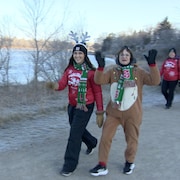 Une femme déguisée en renne de Noël qui fait un salut à la caméra et une autre femme avec un chandail de Noël. 