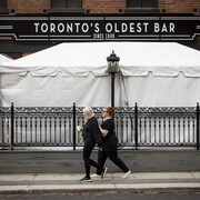 Deux femmes marches devant un bar de Toronto dont la terrasse a été couverte.