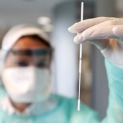 Une technicienne de laboratoire tient un écouvillon dans sa main.