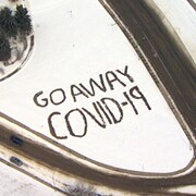 Une vue aérienne d'un message écrit en anglais dans la neige en bordure d'une route signifiant : « Vas-t-en, COVID-19! »