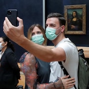 Des visiteurs masqués au musée du Louvre prenant un selfie.