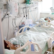 Deux patients intubés couchés dans des lits et des travailleurs de l'hôpital à leur chevet.