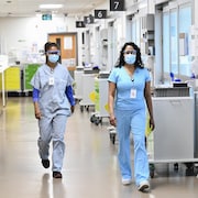 Deux infirmières avec masque et lunettes de protection marchant dans un couloir d'hôpital.