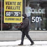 Un homme marche près d'une boutique qui annonce une vente de fermeture.