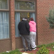 Deux personnes regardent par la fenêtre d'un centre de soins de longue durée pour communiquer avec une personne à l'intérieur.