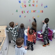 Six jeunes enfants, de dos, collent des dessins de mains sur un mur.