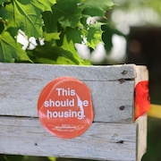Un autocollant rond de couleur orange sur lequel on lit en anglais : « Ceci devrait être un logement ».
