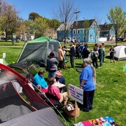 des tentes plantées dans un parc à l'été et avec des citoyens qui discutent