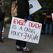 Une personne tient une affiche sur laquelle est écrit, en anglais, que « chaque mort est un échec des politiques sur les drogues ».