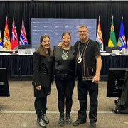 Michelle Corbu, Nelly Jourdain et Mathieu Mckenzie se tiennent debout dans la salle d'audience du CRTC.