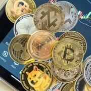 Différentes cryptomonnaies. En arrière plan, une tablette électronique montre l'évolution du cours d'une cryptomonnaie.