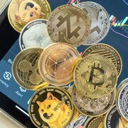 Différentes cryptomonnaies. En arrière-plan, une tablette électronique montre l'évolution du cours d'une cryptomonnaie.