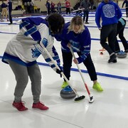 Deux joueuses de curling jouent sur la glace. 