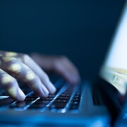 Un homme pose ses mains sur le clavier d'un ordinateur portable dans l'obscurité.