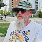 Dan Livers chapeau et lunettes noires regarde la caméra
