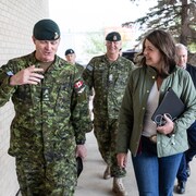 Danielle Smith marche en discutant avec des militaires en uniforme.