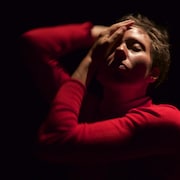 Une interprète en danse touche son visage.  Elle a les yeux fermés. 