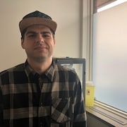 Un jeune homme portant une casquette sourit à la caméra.