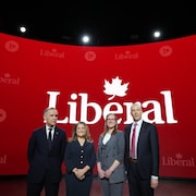 Quatre personnes debout côte à côte devant le logo du parti. 