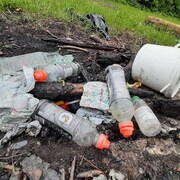 Des déchets de plastique sur un feu de camp éteint.