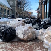 Des sacs à ordure jonchent le sol d'une rue.