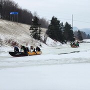 Cinq canots à glace glissent sur la neige poussés par leur équipage. 