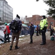 Un policier surveille des gens dans un campement de fortune.