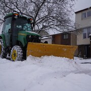 Un tracteur vert pousse de la neige avec sa pelle jaune.