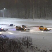 Des véhicules tentent de dépasser les multiples chasse-neige alignés sur l'autoroute alors qu'il neige.