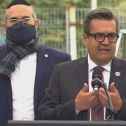 M. Coderre parle devant un micro. On aperçoit le maire de l'arrondissement, Lionel Perez, et candidat de son parti derrière lui.