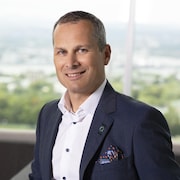 Un homme vêtu d'un veston bleu sourit.