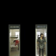 Quatre vidéos verticales projetées sur un mur noir montrent des femmes dans leurs cellules de prison. 