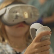 Une enfant est équipée d'un casque de réalité virtuelle et d'une manette.