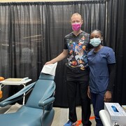 Deux personnes en tunique médicale et portant des masques chirurgicaux posent à côté d'une chaise de dentiste.