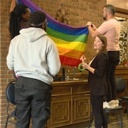 Des personnes hissent le drapeau de la communauté LGBTQ+ dans un espace communautaire en Alberta.