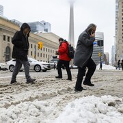 Des piétons traversent la rue dans la neige à moitié fondue, sous un ciel gris.